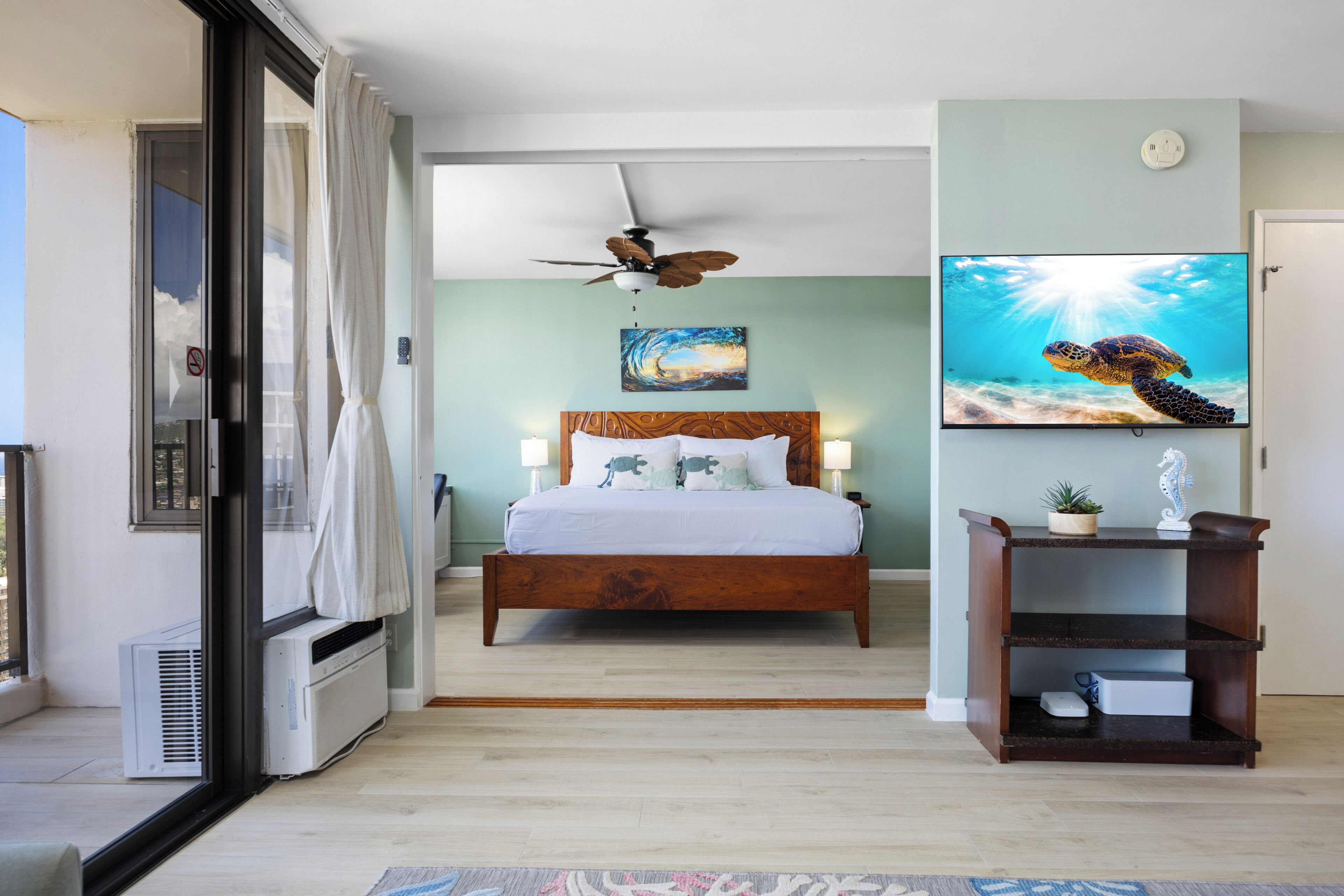 A bedroom with a bed, ceiling fan, artwork, and a TV.