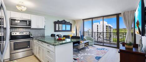 A modern kitchen with a large island, stainless steel appliances, and a view to a balcony.