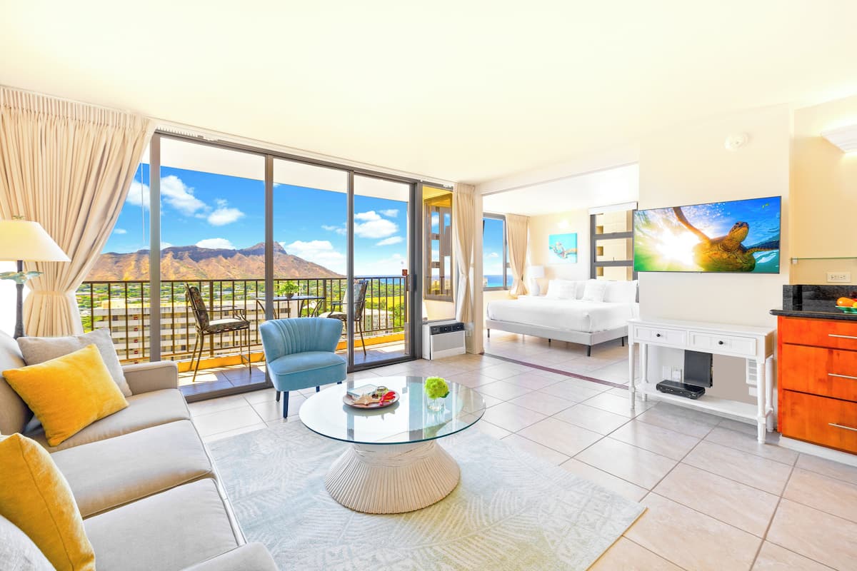 Quarto de hotel moderno com varanda, sofá, mesa de centro, televisão e escrivaninha.