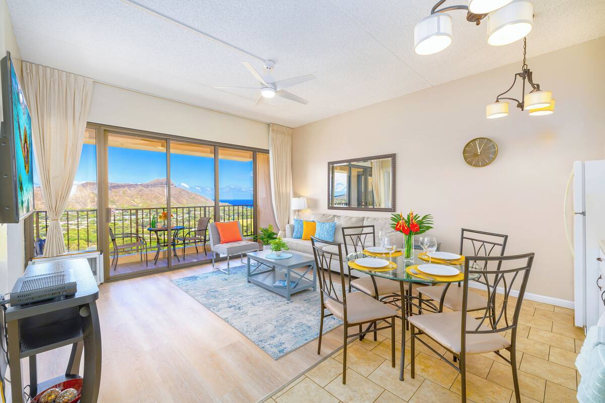 Un balcon spacieux offrant une vue sur les montagnes, un coin repas avec une table dressée pour quatre personnes et un ventilateur de plafond.