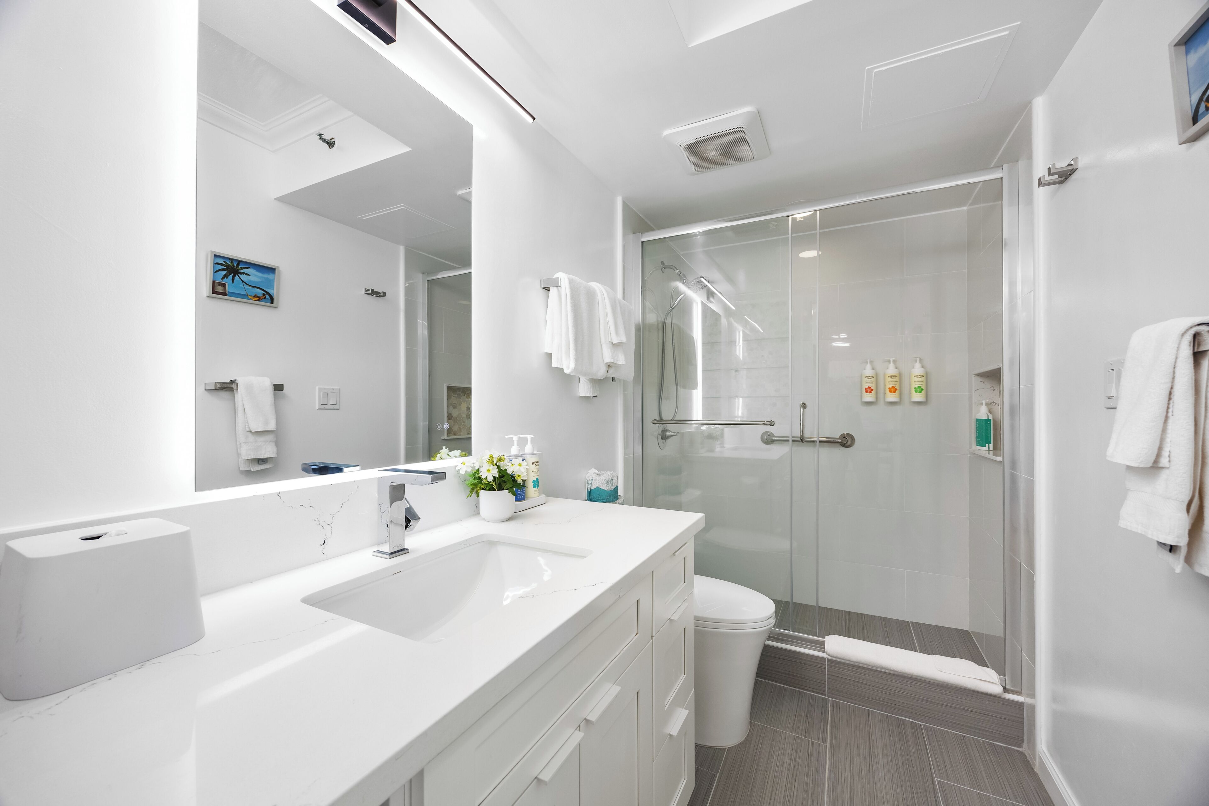 A modern bathroom with a large mirror, a white sink, a glass shower enclosure, and a white toilet.