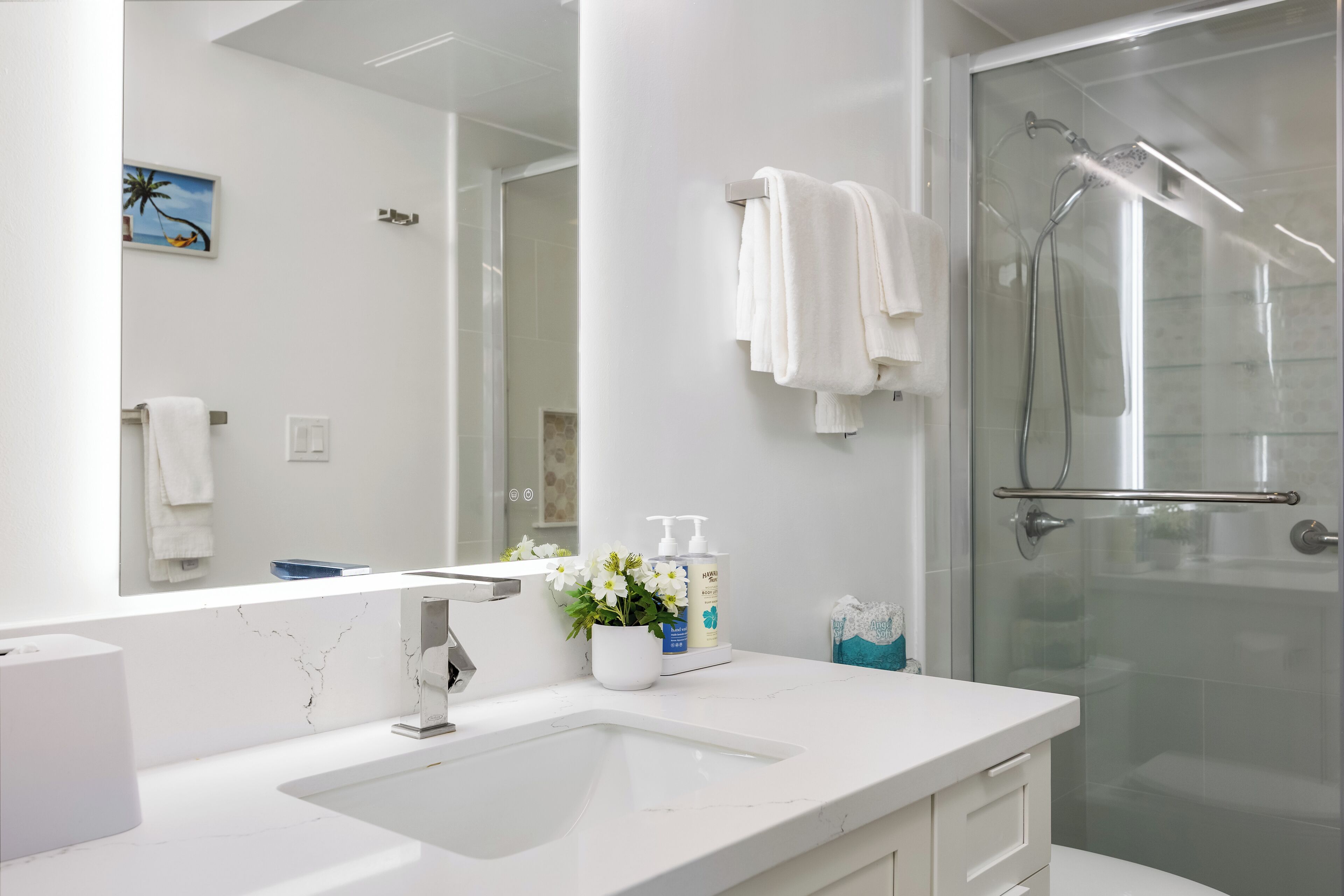 A modern bathroom with a white sink, a glass shower enclosure, and a large mirror.
