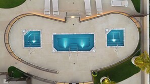 Vista aérea de una zona de piscina con tres albercas, un área de descanso techada y un deck circundante.