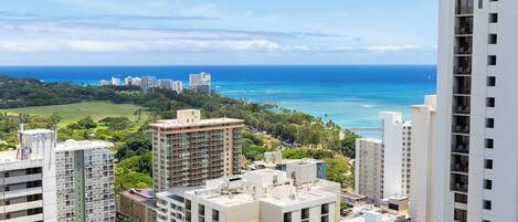 A high-rise building with multiple floors, surrounded by other buildings and a view of the ocean.