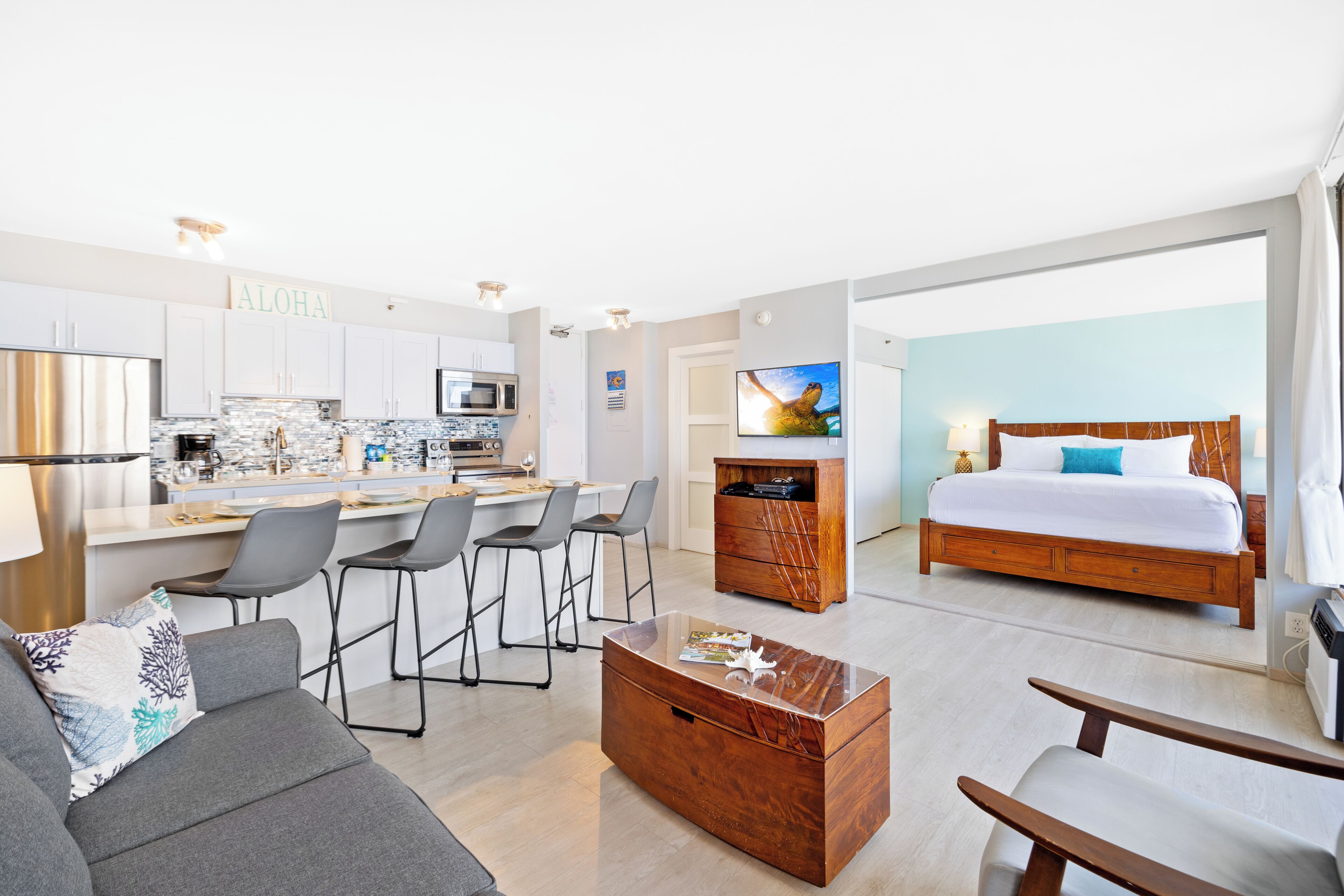 A modern hotel room with a kitchen area, a dining space, and a large bed.