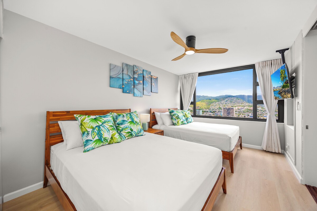A hotel room with two beds, a ceiling fan, a city view, and artwork on the wall.