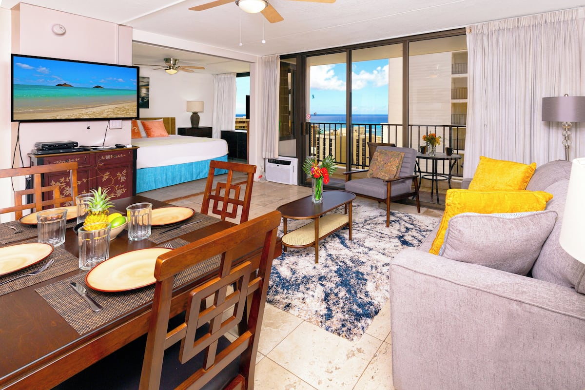 A hotel room with a balcony, a dining area, and a living room.