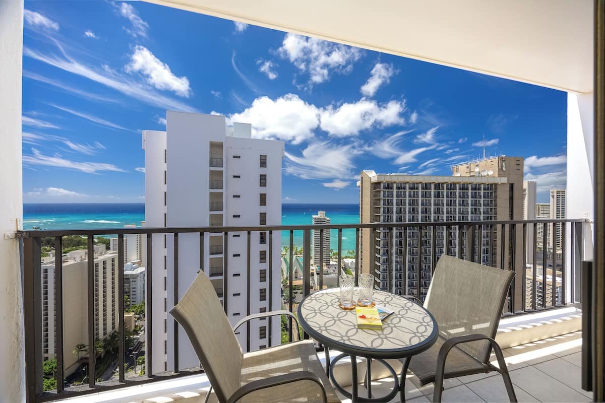 A balcony with two chairs and a table, overlooking a cityscape and the ocean.
