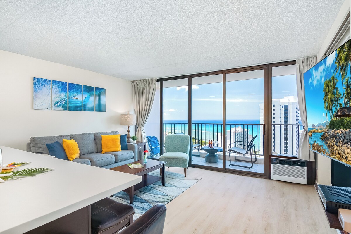 A modern living room with a balcony overlooking the ocean, a dining area, and a large window with curtains.