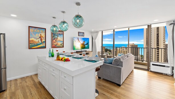 A modern apartment with a kitchen, dining area, and a balcony with a view of the ocean.