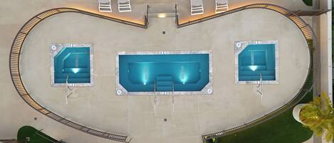 An aerial view of a swimming pool area with three pools, a covered seating area, and a surrounding deck.
