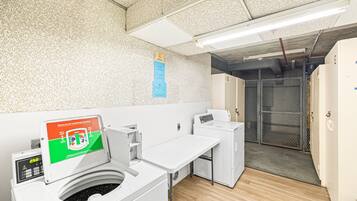 A laundry facility with industrial washing machines, a control panel, and a metal gate leading to a storage area.