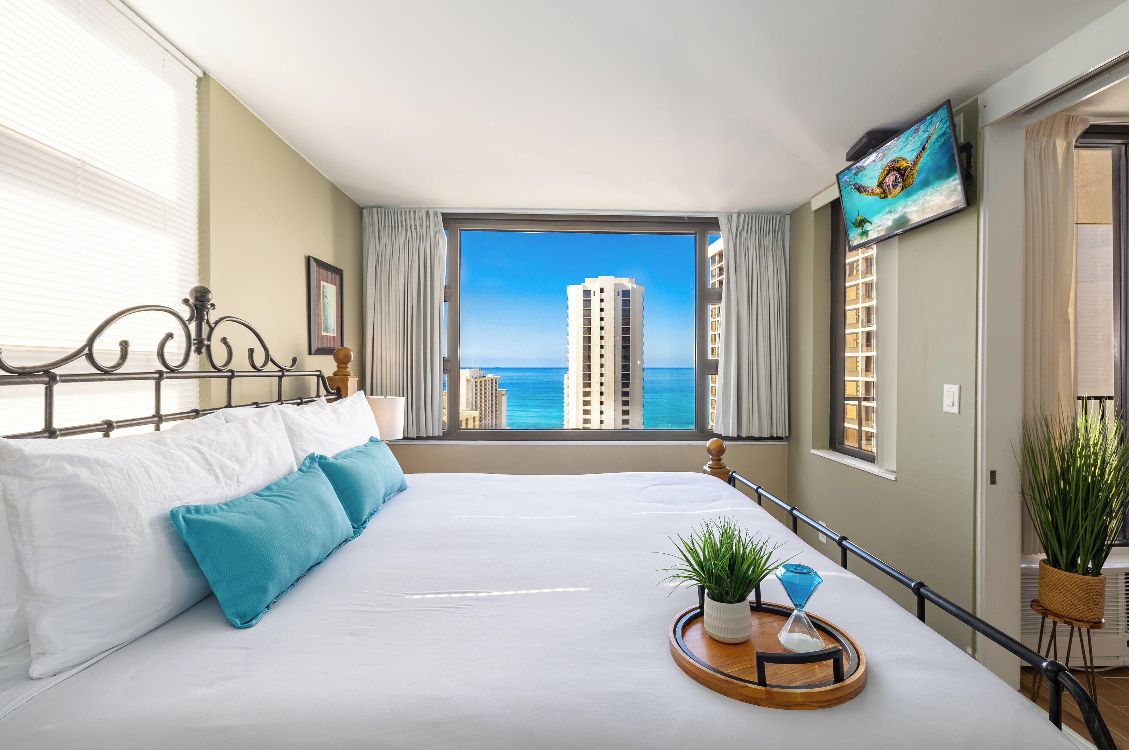 Habitación de hotel con una cama grande, un televisor en la pared y vistas al océano y edificios.