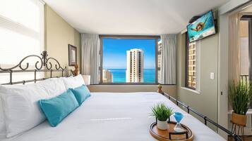 Habitación de hotel con una cama grande, un televisor en la pared y vistas al océano y edificios.