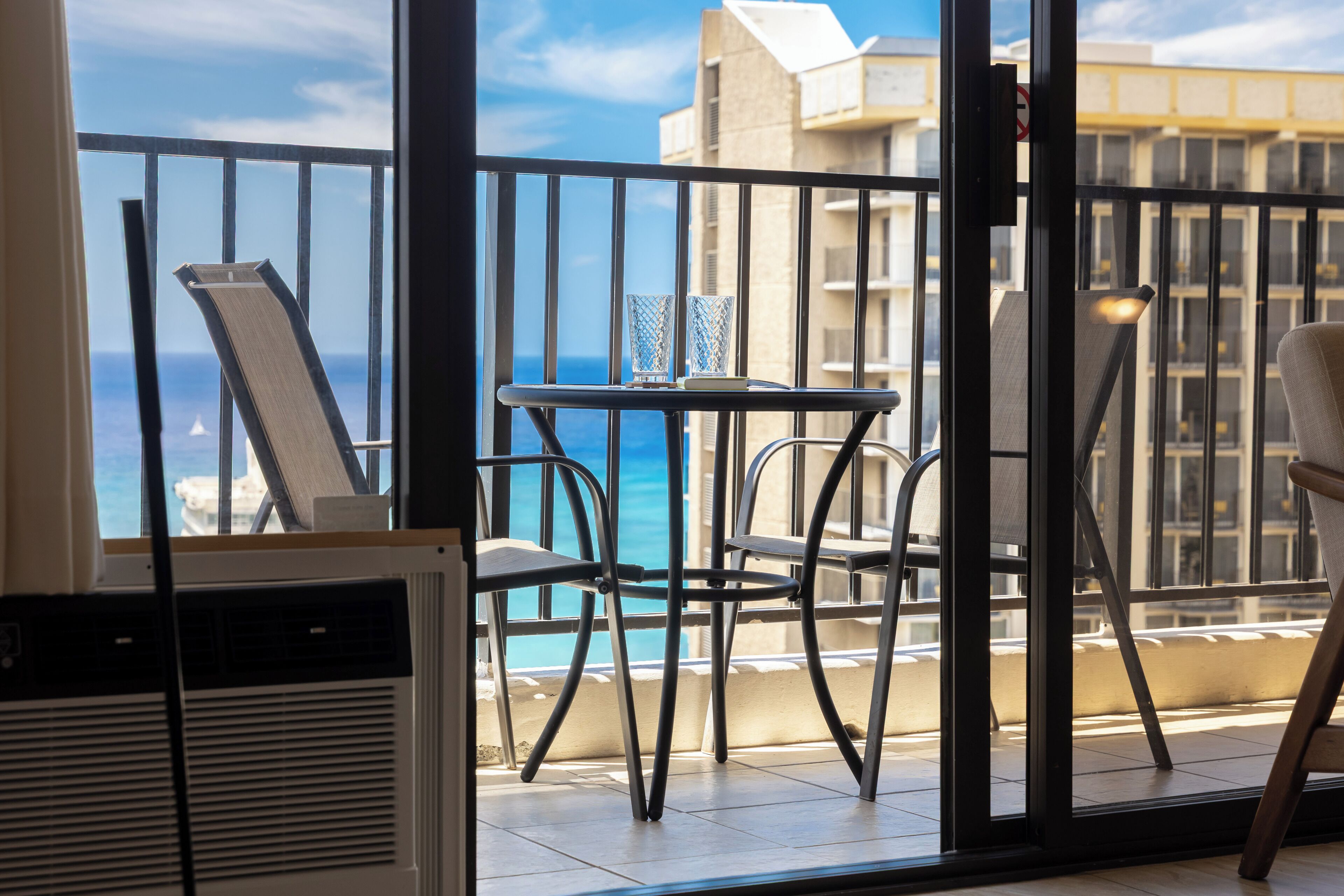 A balcony with a view of the ocean, a table with chairs, and a chair.