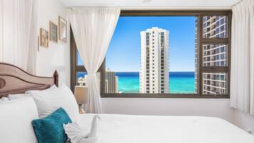 A hotel room with a large window offering a view of a tall building and the ocean.