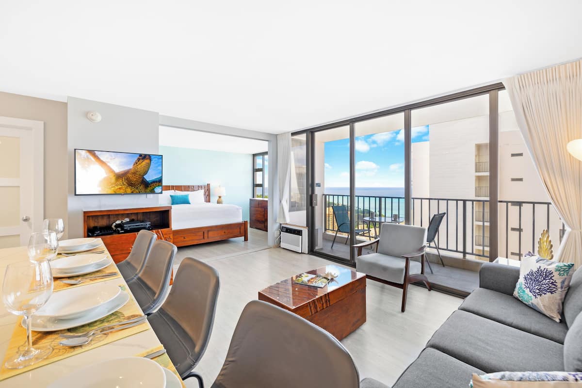 A modern hotel room with a balcony, a bed, a TV, a dining area, and a sofa.
