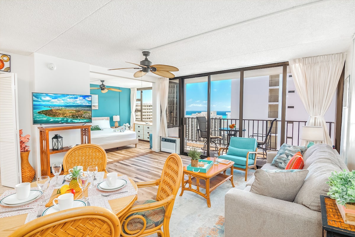 A spacious living room with a large TV, dining area, and a balcony with a view.
