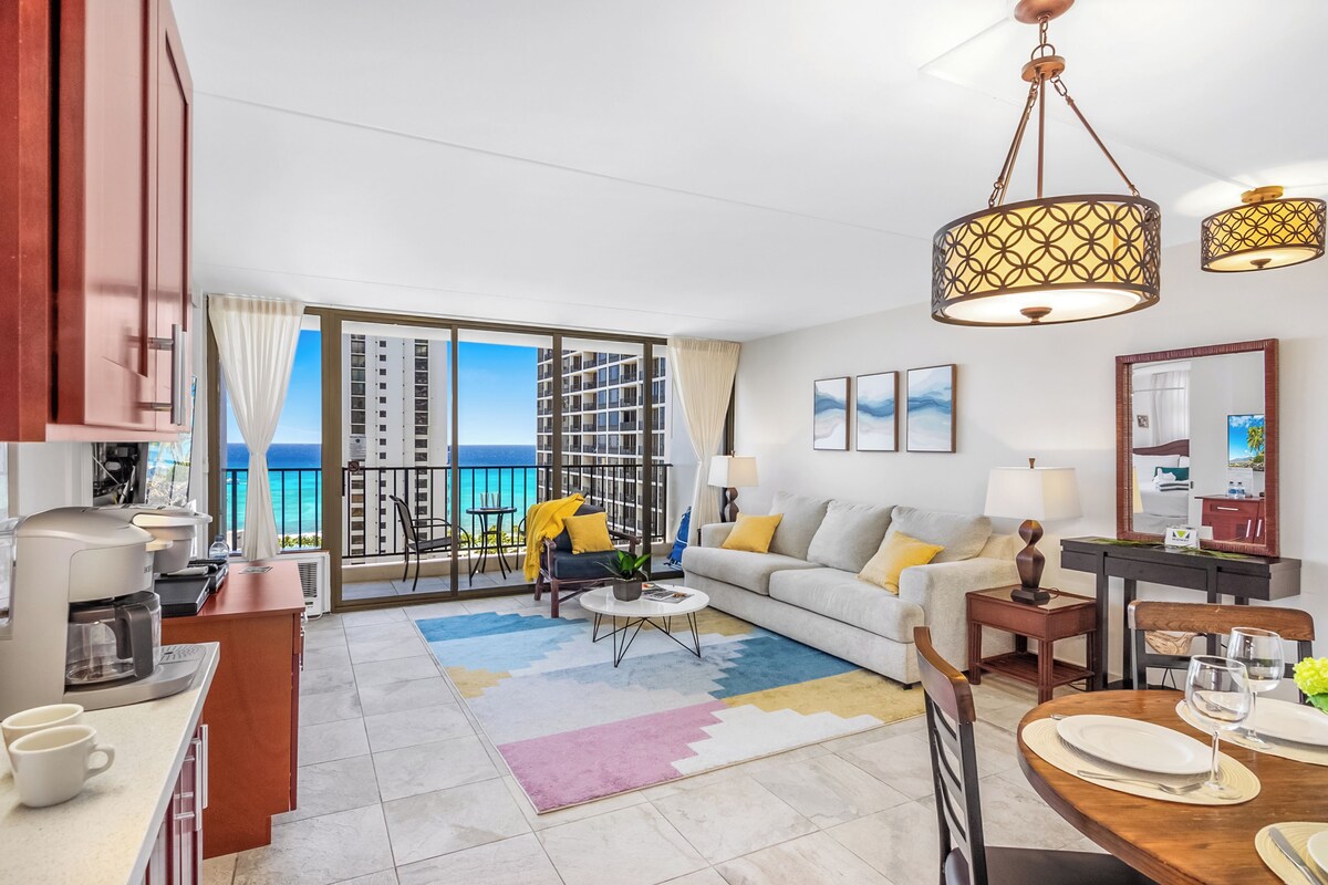 A modern living room with a balcony, a coffee station, a dining area, and a view of the ocean.