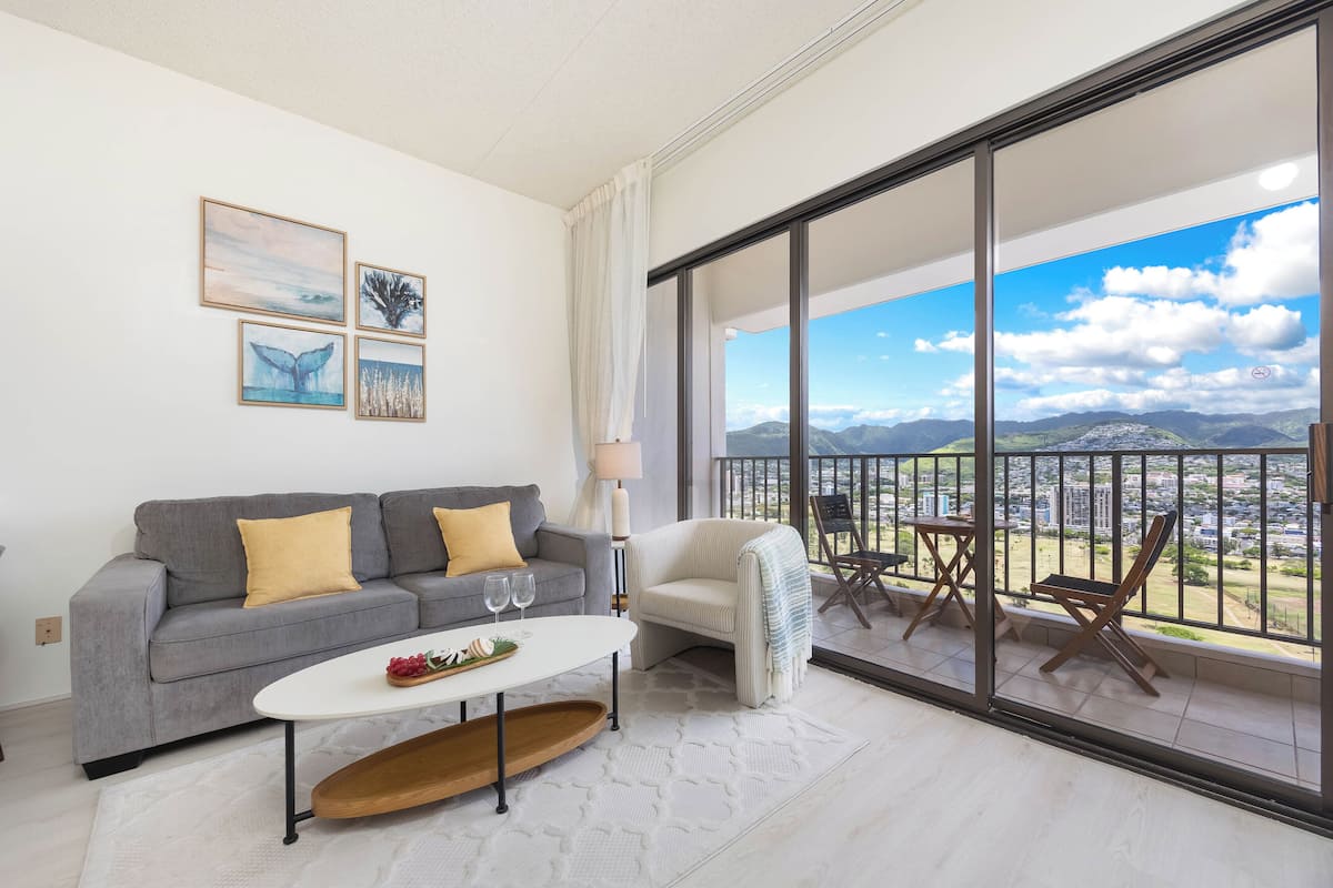 A modern living room with a grey sofa, a white coffee table, and a balcony with a city view.