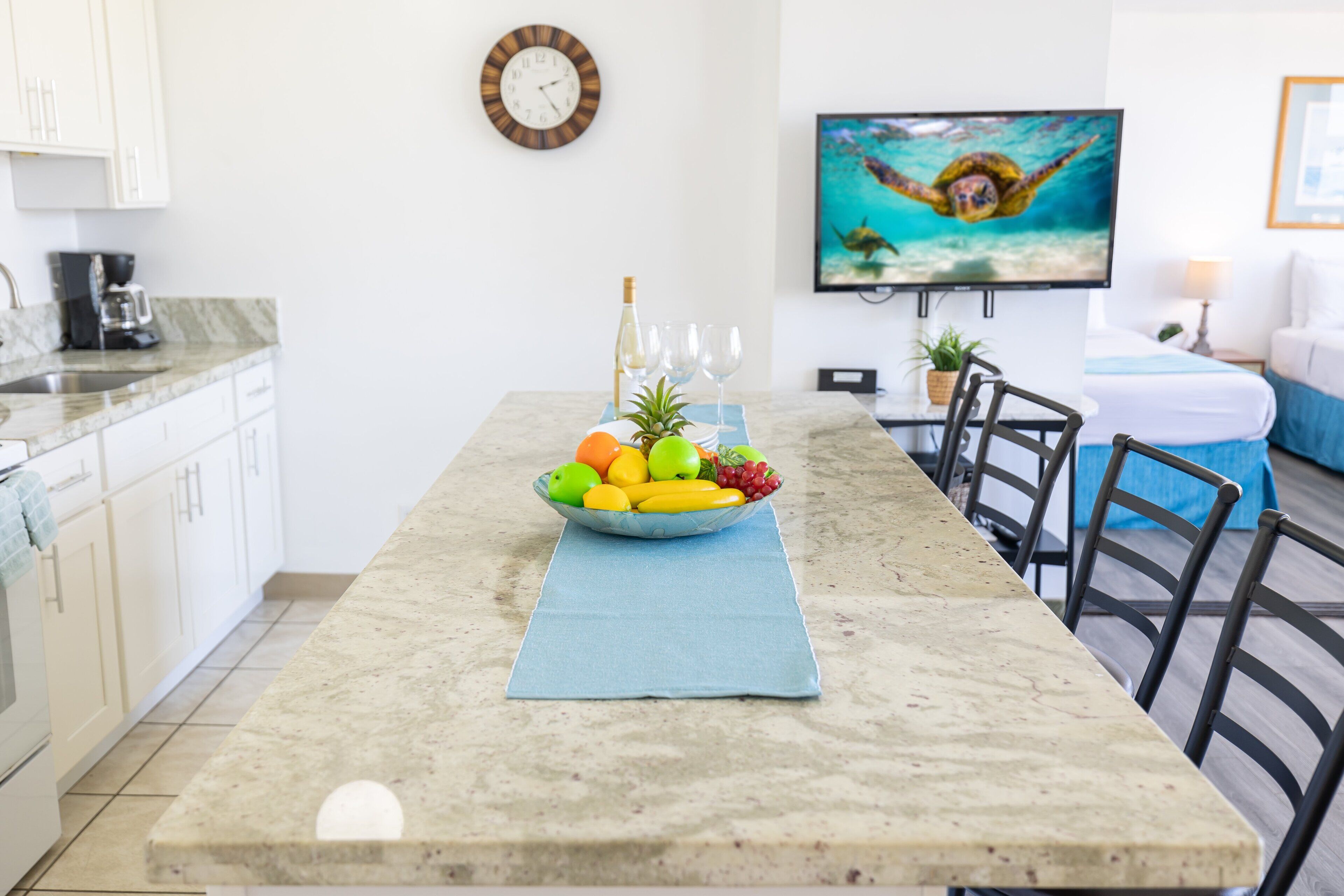 A dining area with a marble table, a bowl of fruit, a bottle, and a clock on the wall.