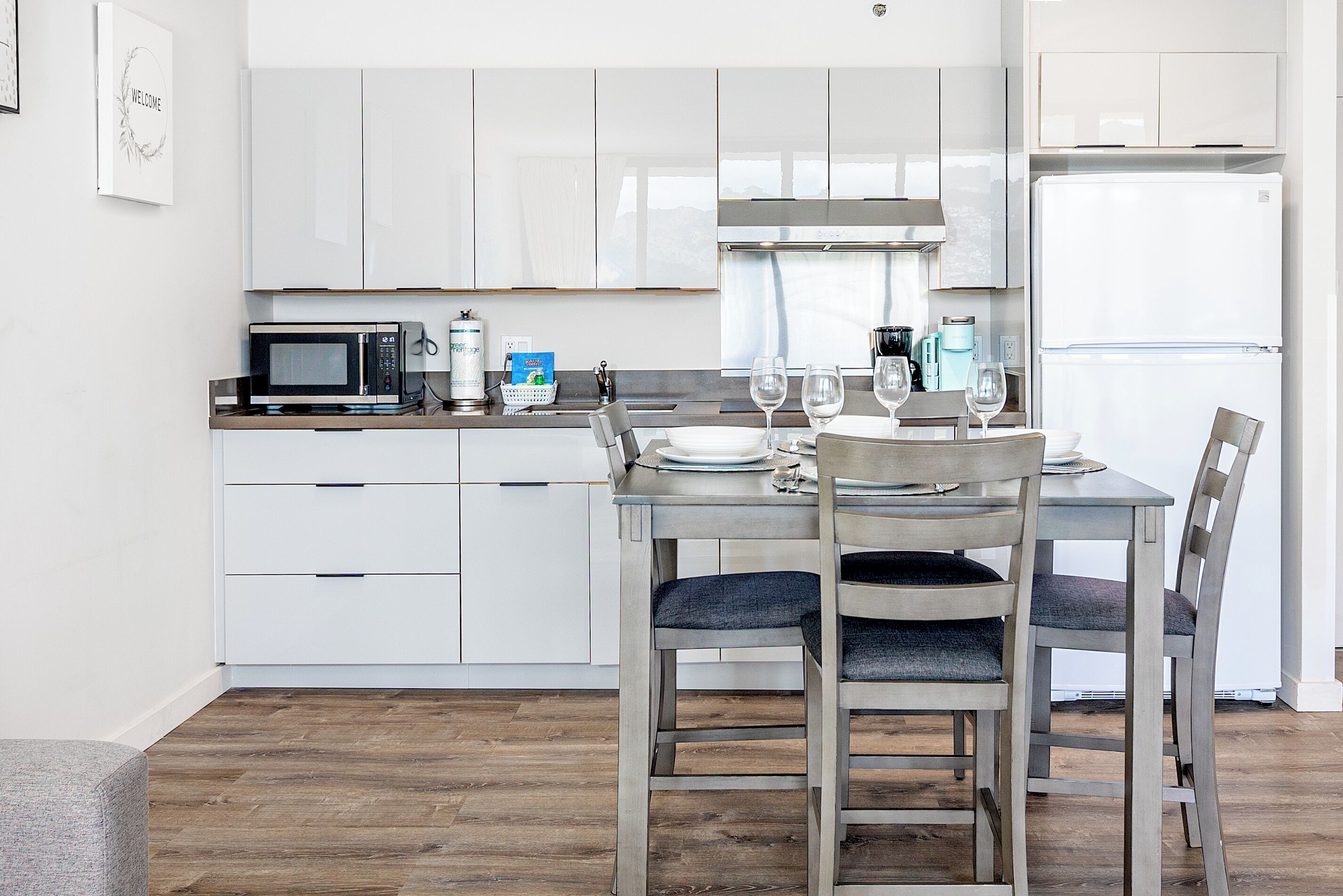 A modern kitchen with white cabinets, a microwave, a refrigerator, and a dining table with chairs.