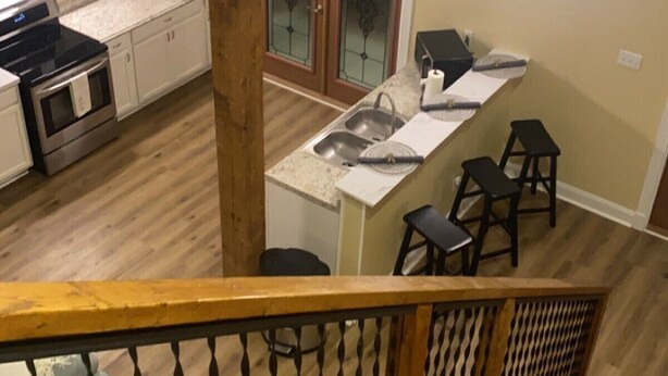 Een moderne keuken met een centraal eiland, een eethoek met barkrukken en een trap met houten leuning.