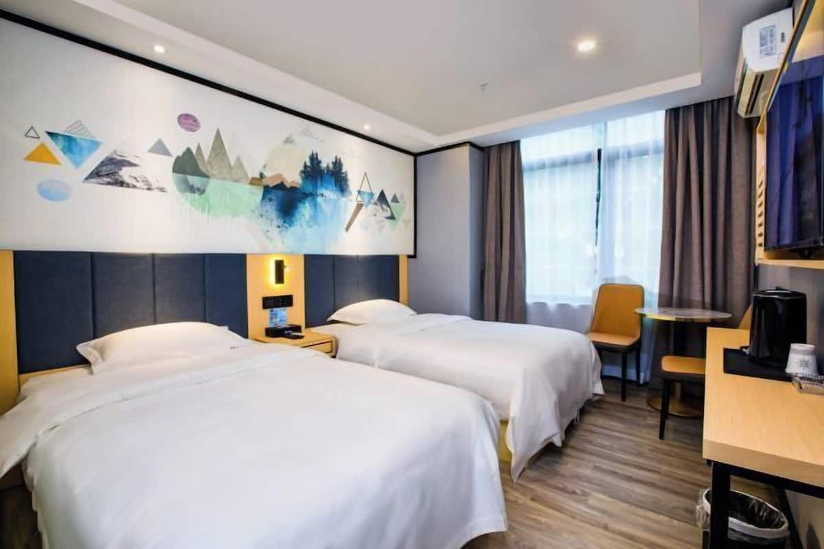 A hotel room with two beds, a desk, a chair, a coffee machine, and a large abstract painting on the wall.
