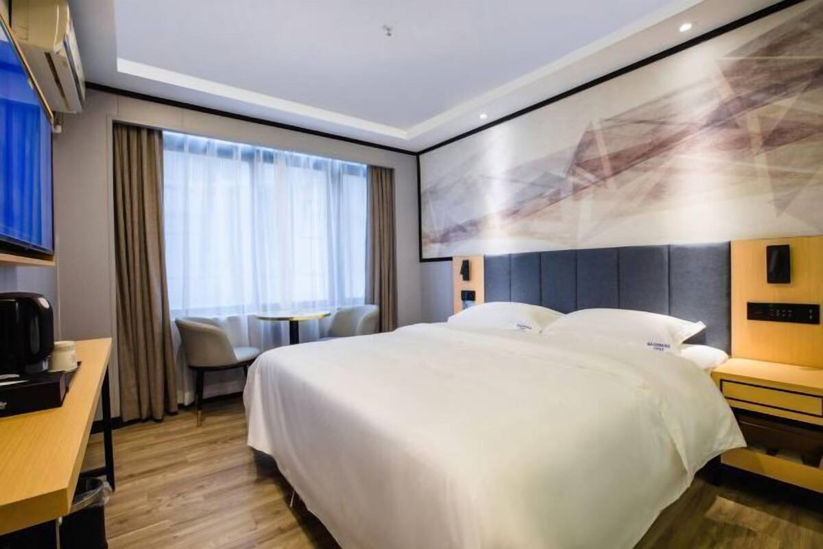 A hotel room with a large bed, a desk with a chair, a TV, and a window with curtains.