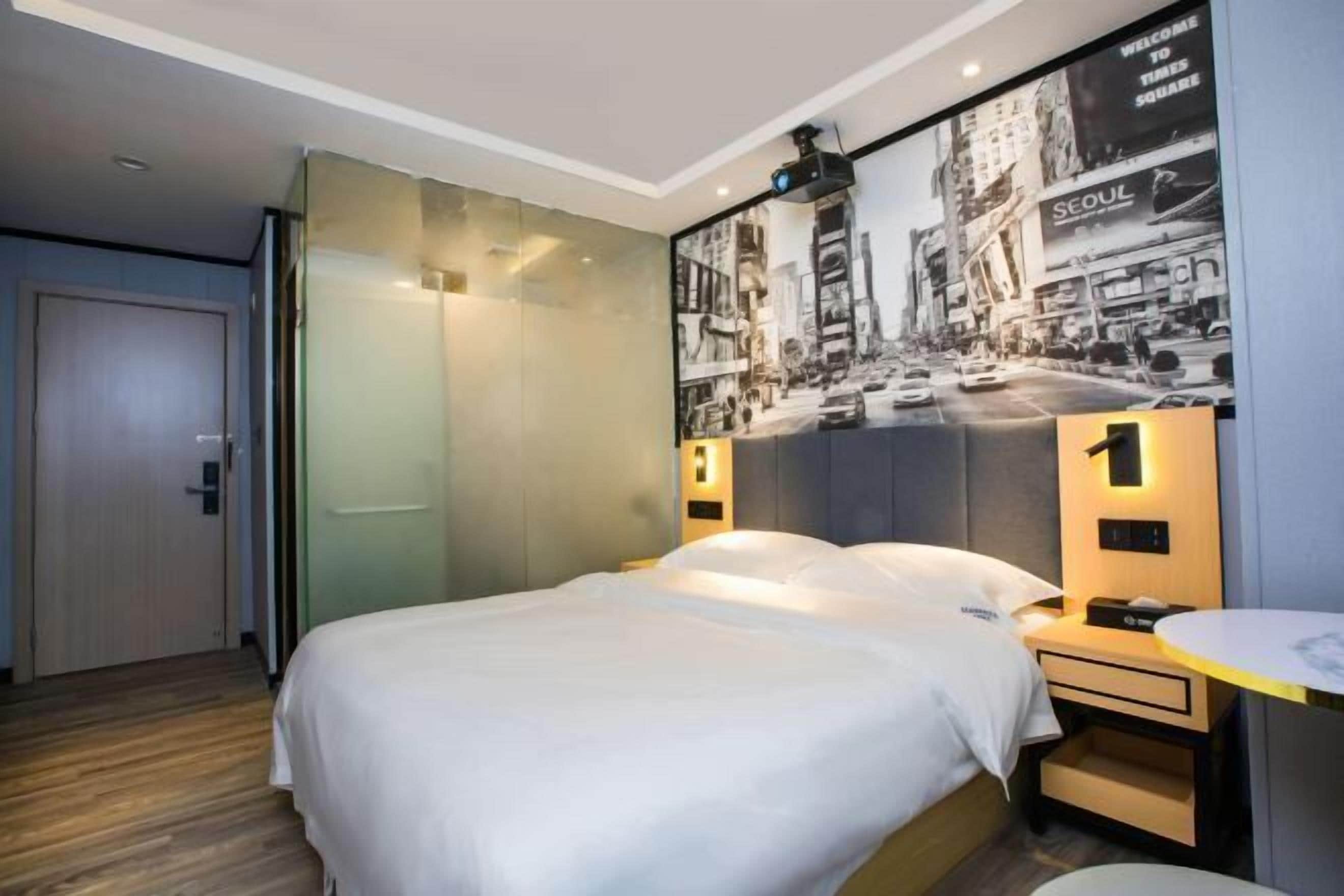 Ett hotellrum med en säng, ett nattduksbord, en väggmonterad TV och en affisch med motiv från Seoul.