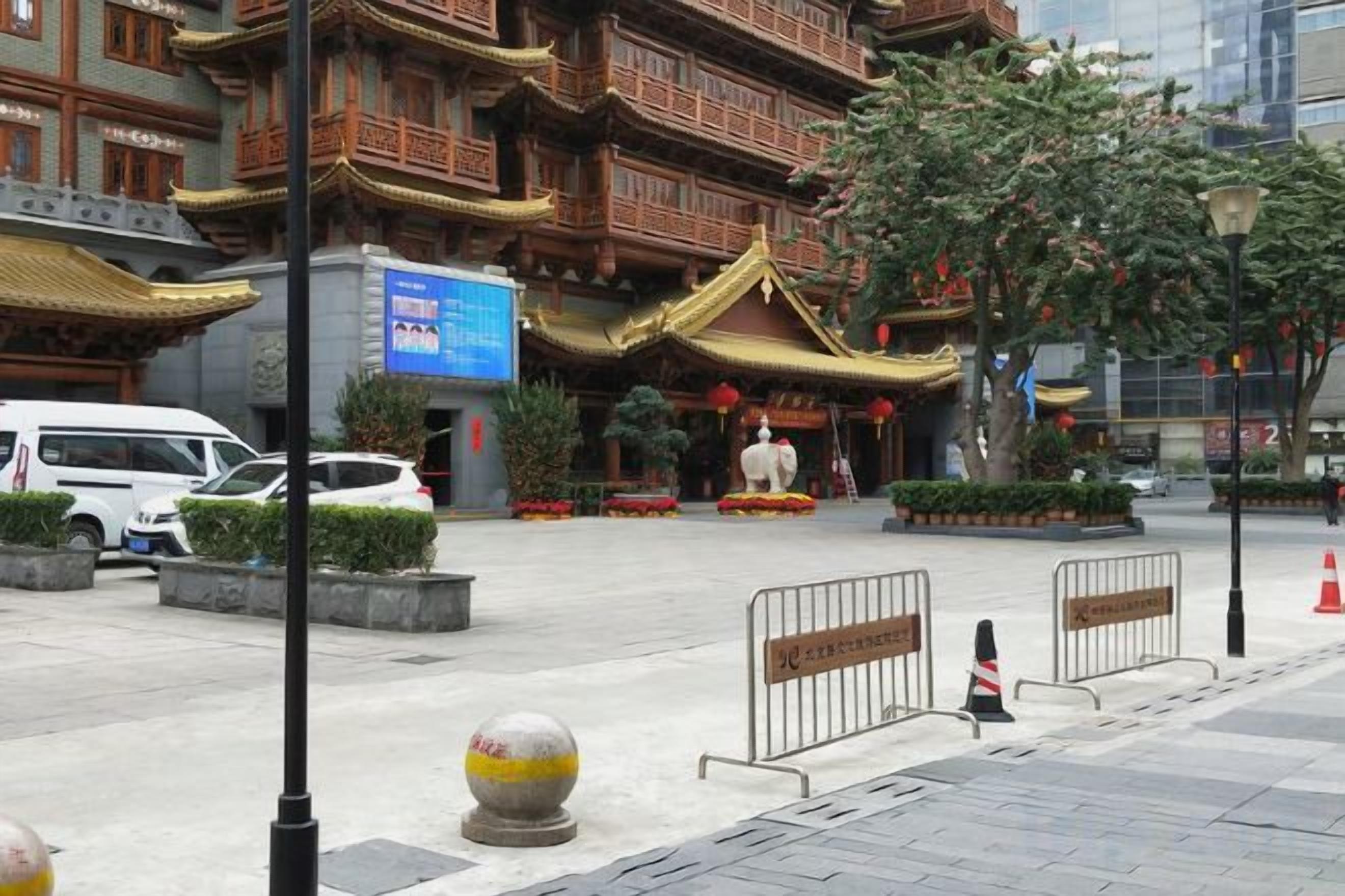 A traditional building with a golden roof, surrounded by greenery and a paved area with bollards.