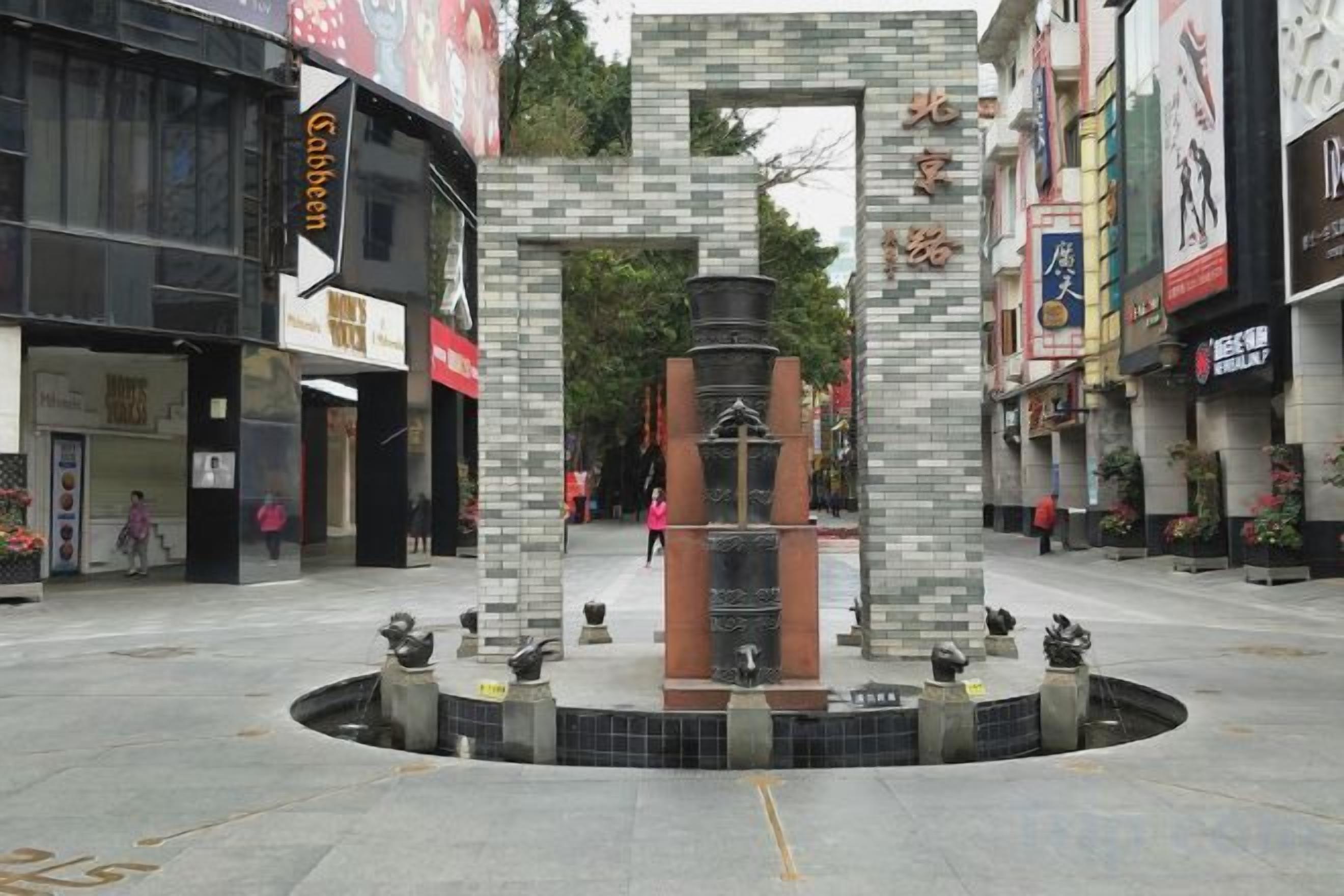 Une place publique avec une fontaine centrale, entourée de bâtiments abritant différents commerces.