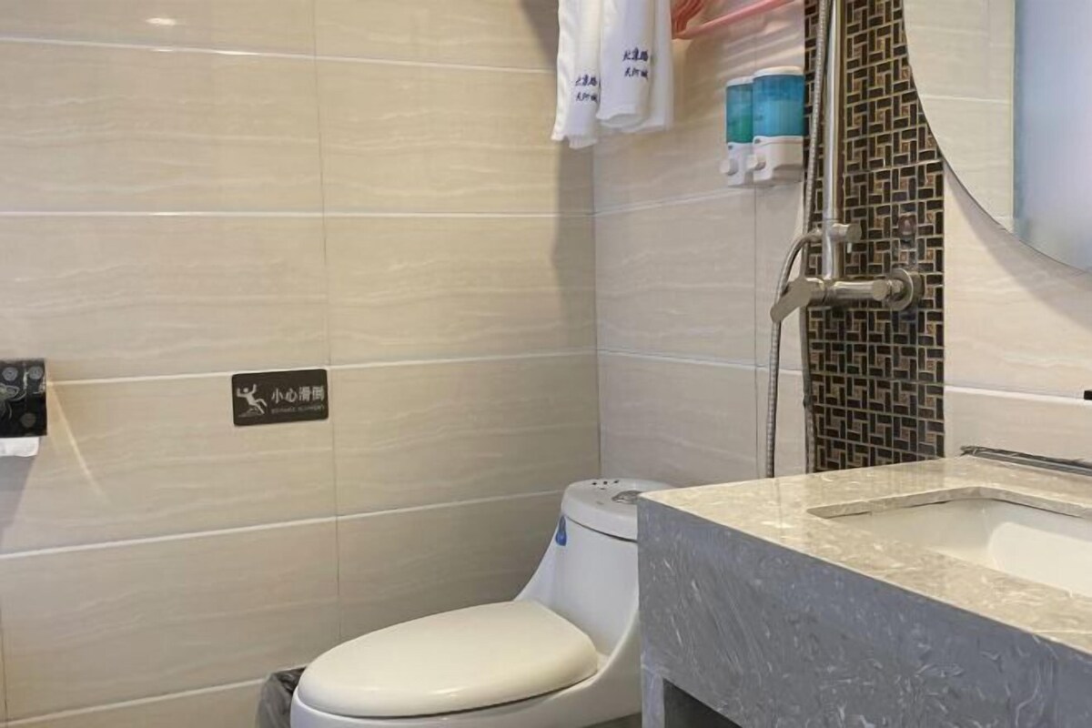 A bathroom with a toilet, a sink, and a shower. There are towels hanging on the wall and a sign indicating a baby changing area.