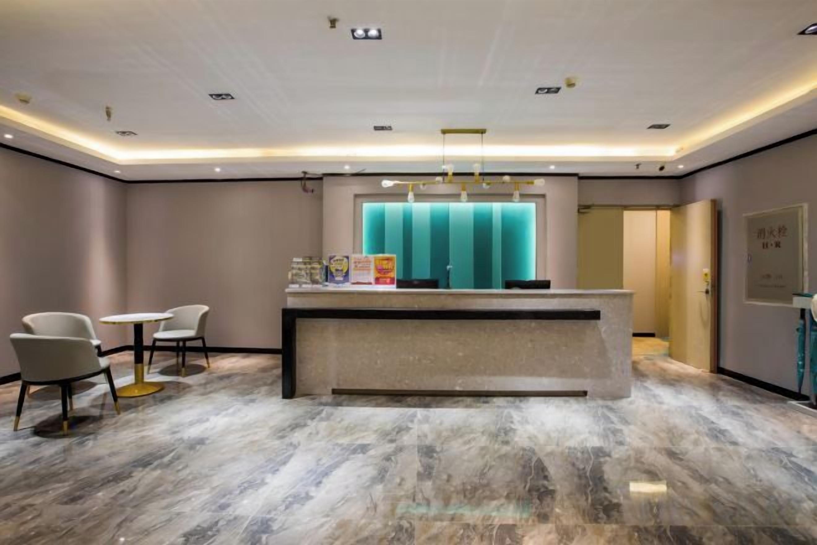 Zona de recepción de un hotel con suelo de mármol, mostrador de recepción y dos sillones.