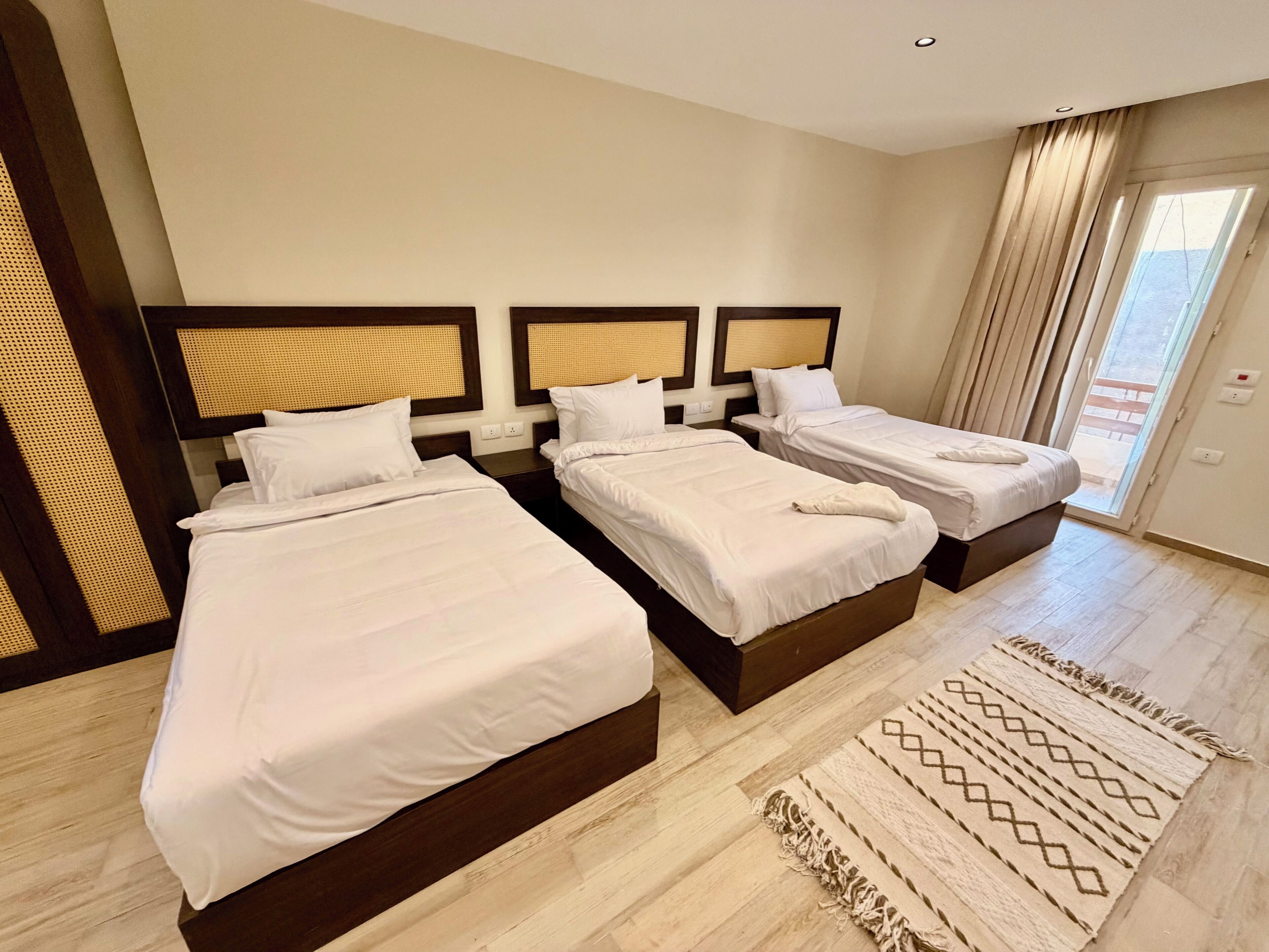 Habitación de hotel con tres camas, un ventanal con cortinas y una alfombra estampada.