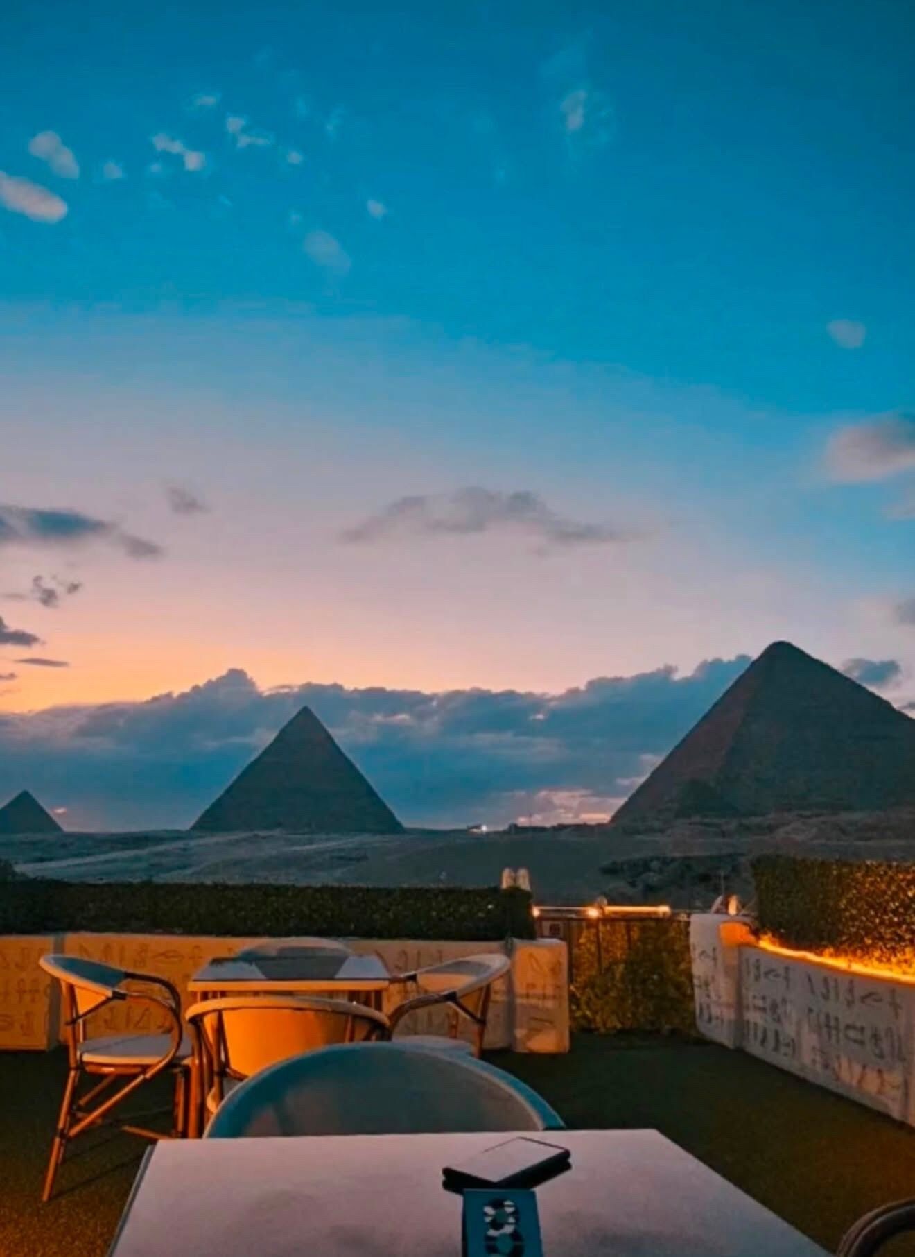 A dining area with tables and chairs, overlooking a landscape with pyramids.