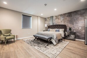 Une chambre à coucher moderne avec un grand lit, un banc, une chaise, une petite table et une table de chevet avec une lampe.
