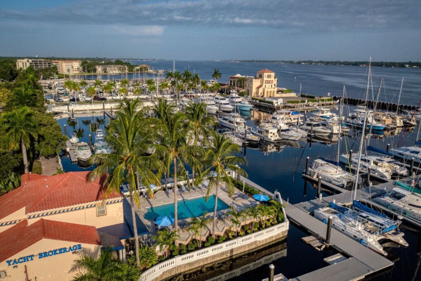 Un puerto deportivo con numerosas embarcaciones amarradas, una piscina y un edificio con la leyenda 'Yacht Brokerage'.