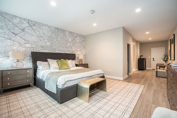 A bedroom with a large bed, a nightstand, a dresser, and a patterned rug.