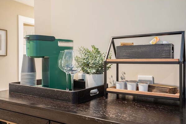 A kitchen counter with a coffee maker, a glass, a potted plant, and a shelf with various items.