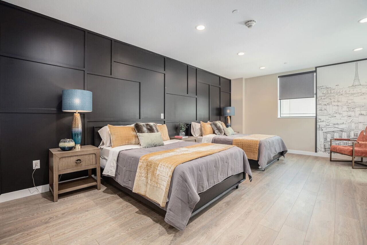 A modern bedroom with two beds, dark paneling on the wall, and a cityscape mural.