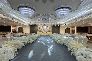 A banquet hall with a central aisle, round tables, and a chandelier.