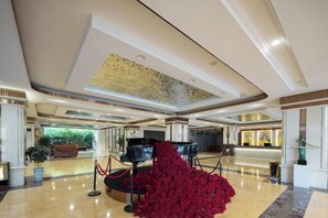 Eine geräumige Lobby mit einem Flügel, einer roten Blumenkomposition und einer Rezeption.