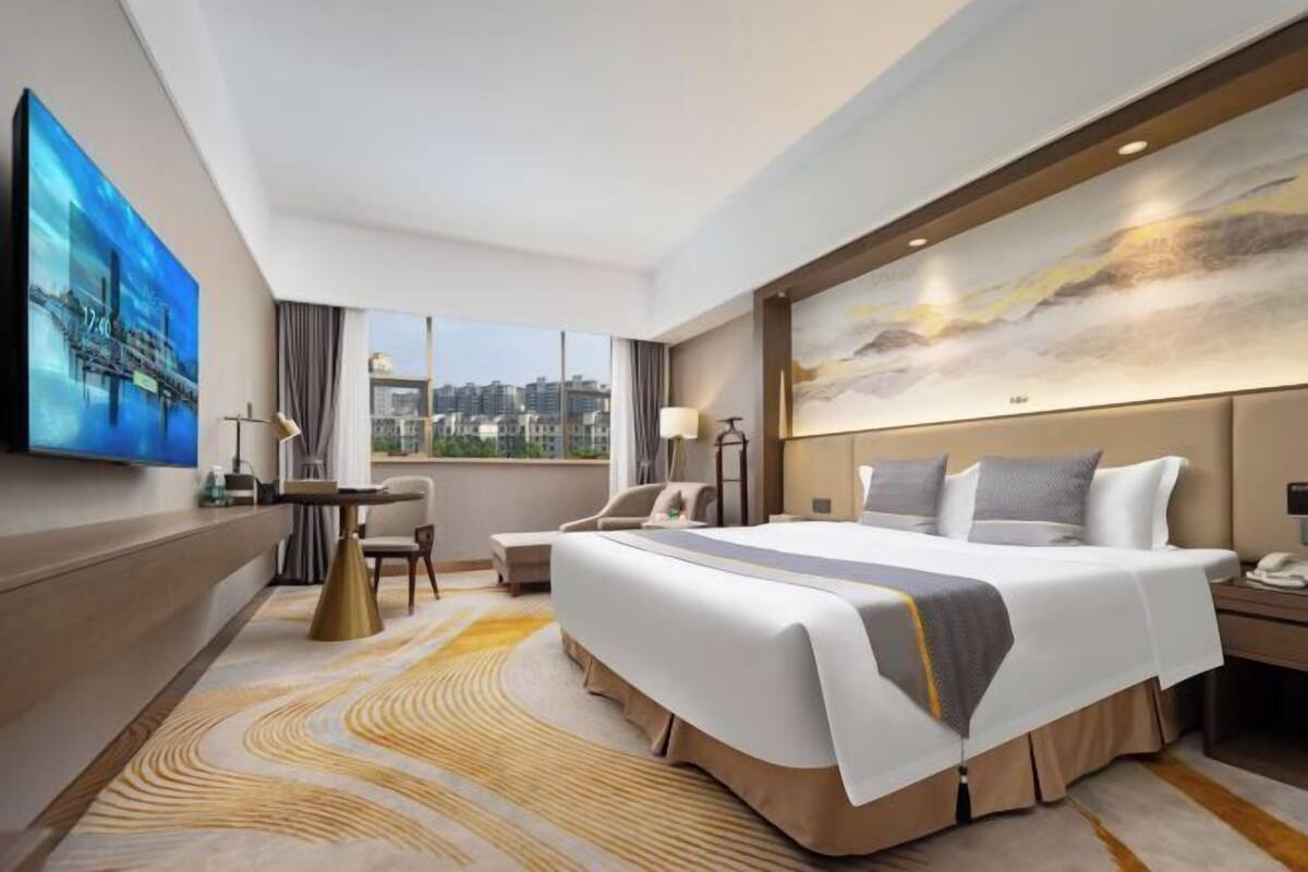 A modern hotel room with a large bed, a desk, a chair, and a TV on the wall.