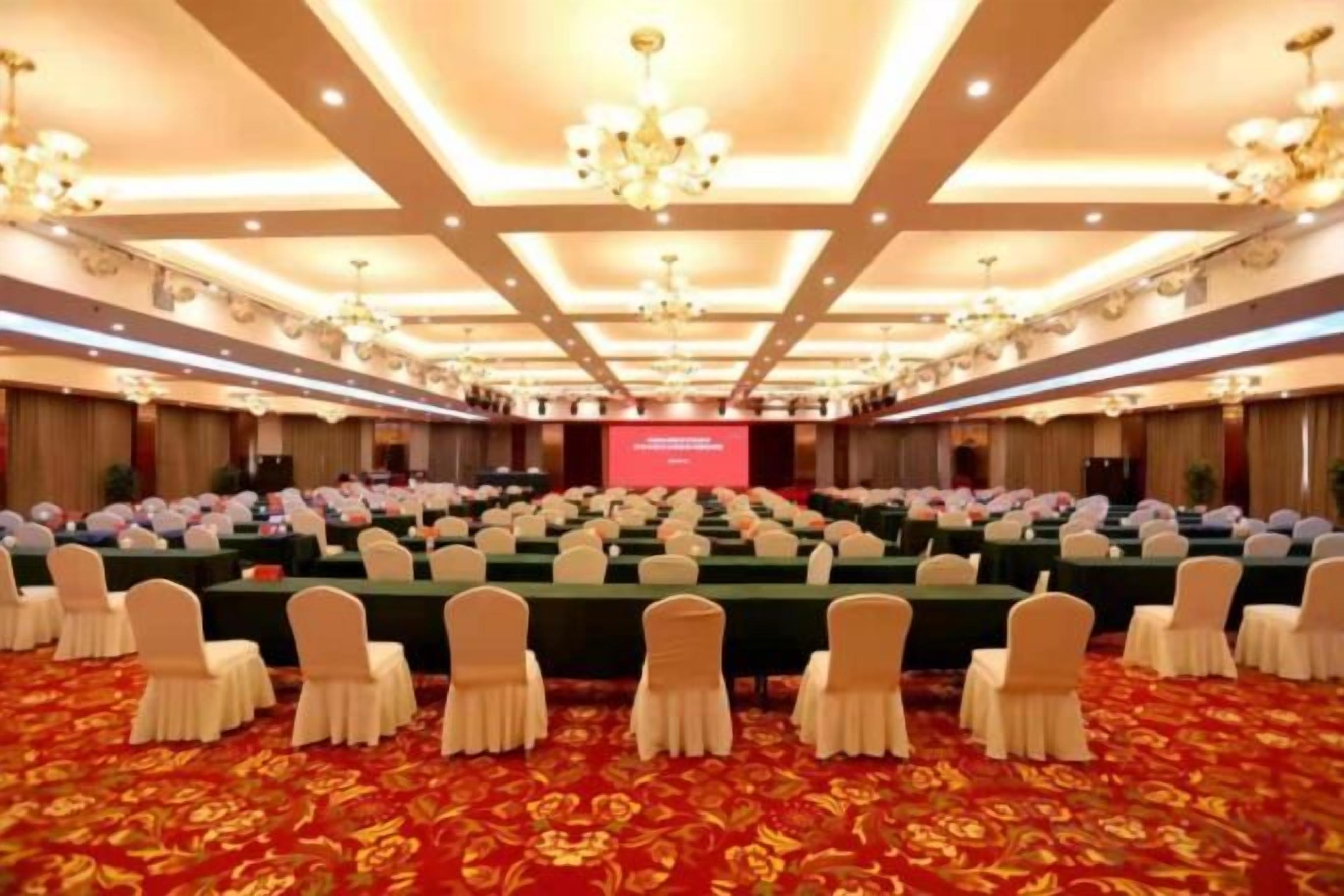 A conference room with rows of tables and chairs, a stage with a screen, and a red carpet.