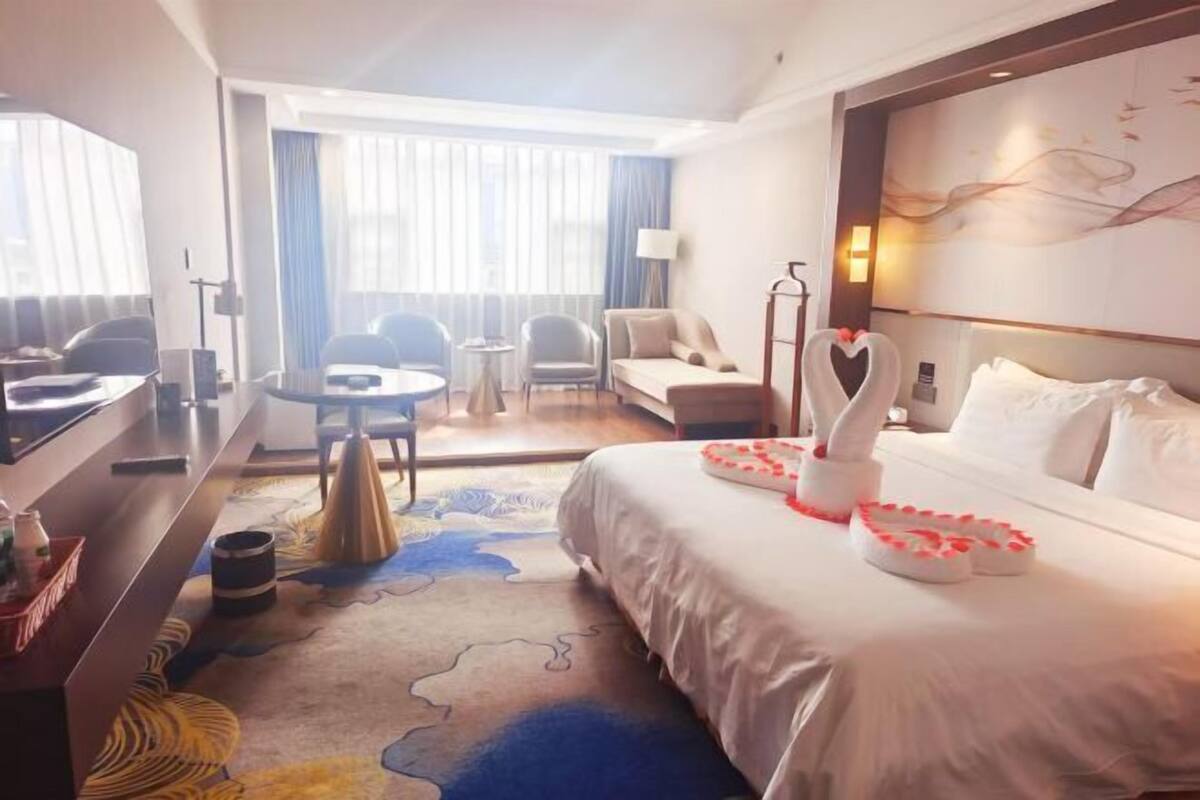 A hotel room with a bed, a desk, a chair, a small table, and a view of the outside.