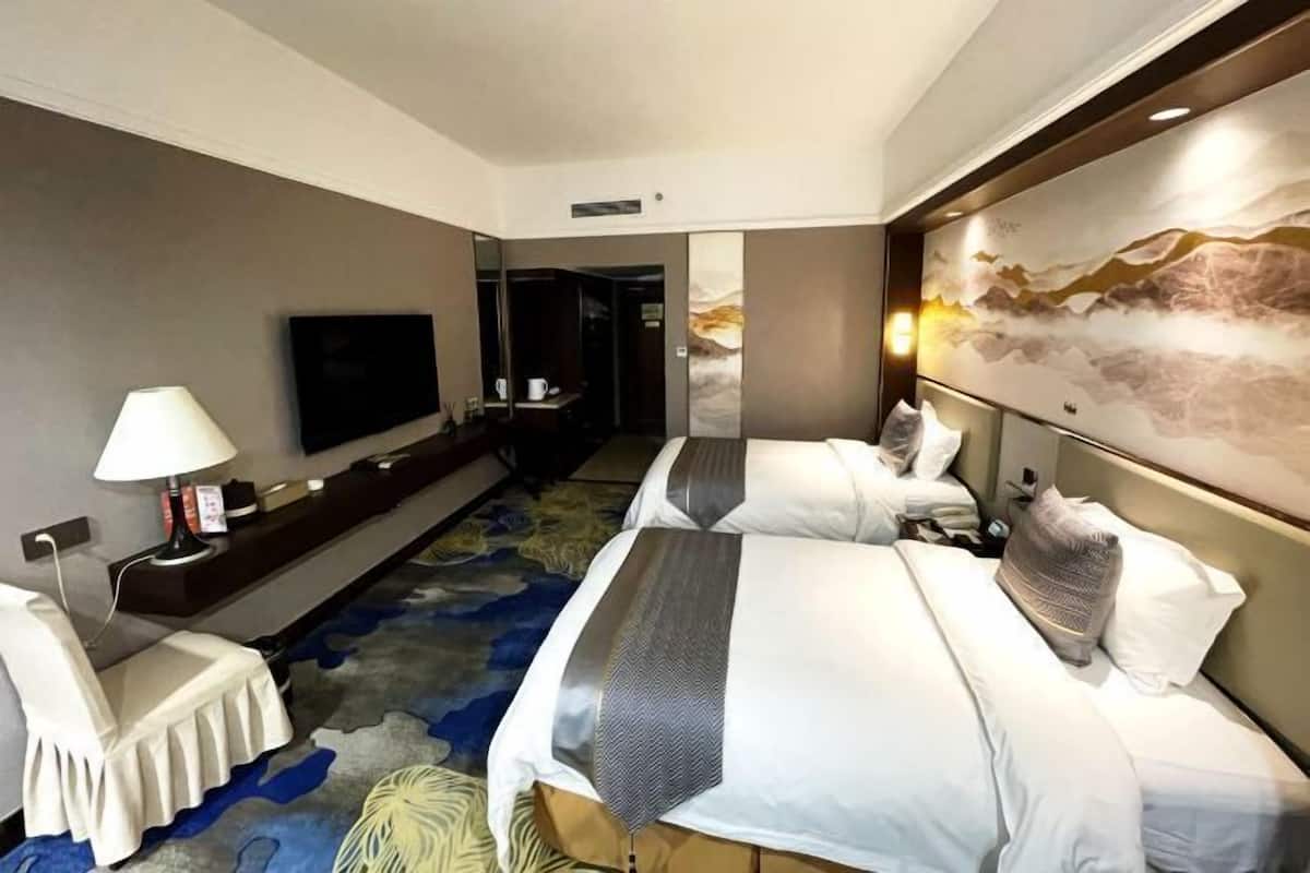 A hotel room with two beds, a flat-screen TV, a desk, and a large abstract painting on the wall.