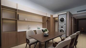 A modern kitchen with built-in appliances, a dining area with a wooden table and chairs, and a laundry room with stacked washing machines.