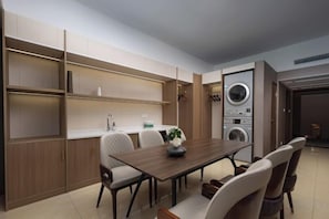 Een moderne keuken met inbouwapparatuur, een eethoek met een houten tafel en stoelen, en een wasruimte met gestapelde wasmachines.