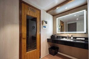 Une salle de bain moderne avec une porte en bois, un grand miroir, un lavabo et une poubelle.